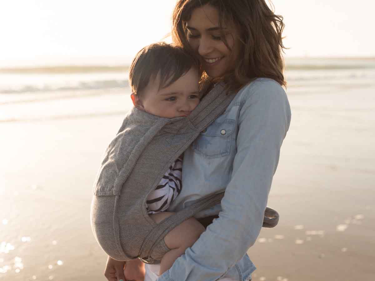 mama ze swoim dzieckiem w nosidle na plaży