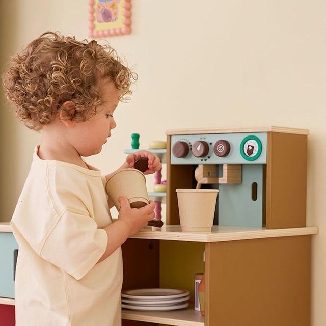 Zbliżenie na drewniany ekspres do kawy z kolbą, przyciskami i wskaźnikiem ciśnienia w zabawkowej kawiarni Kid's Concept
