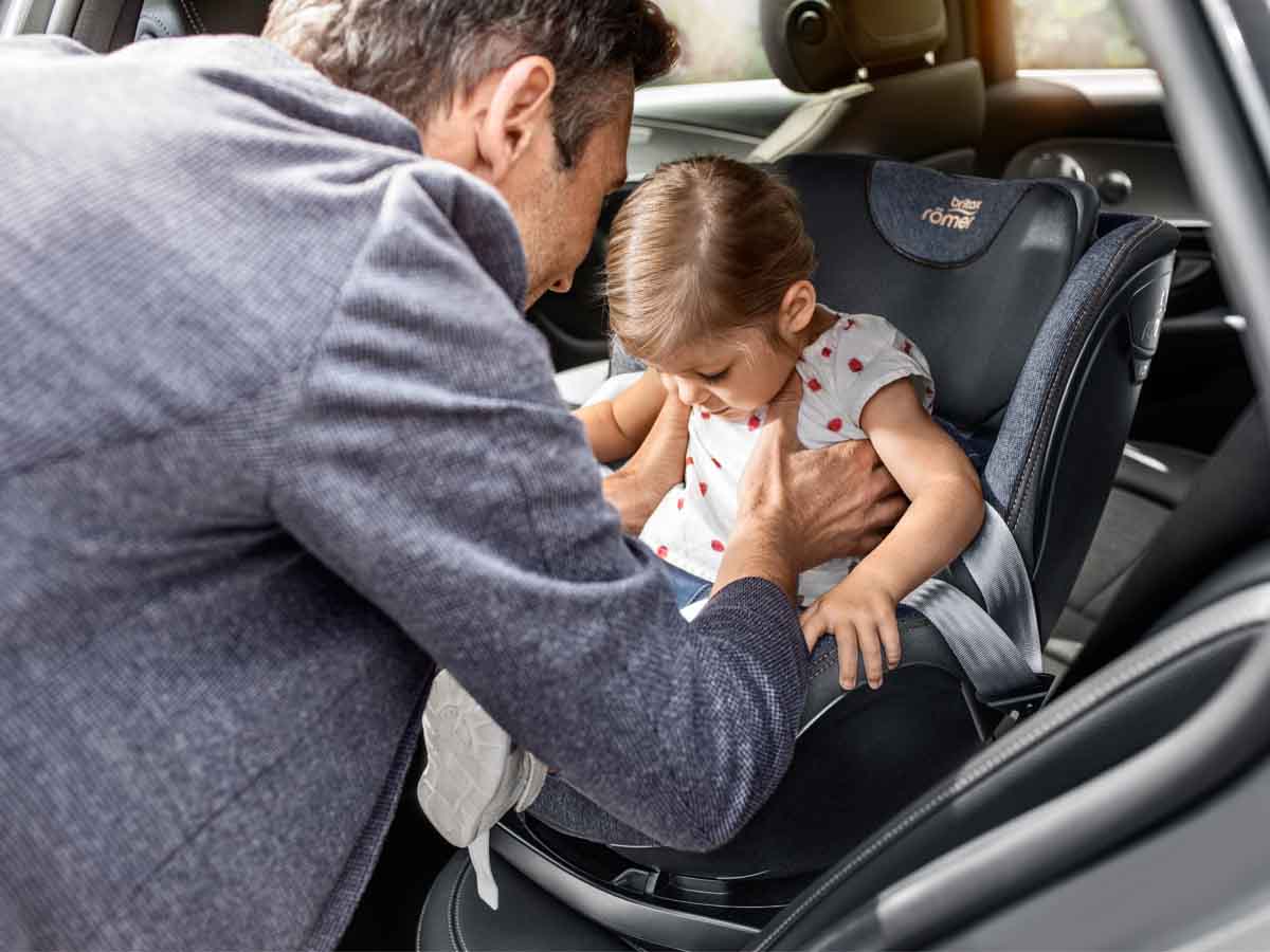 Tata wkłada córkę do fotelika samochodowego